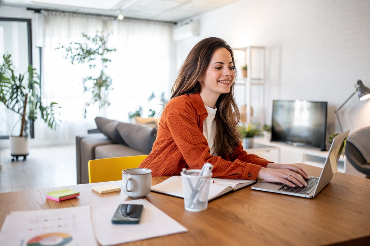 Woman working from home at a wooden table with coffee and laptop