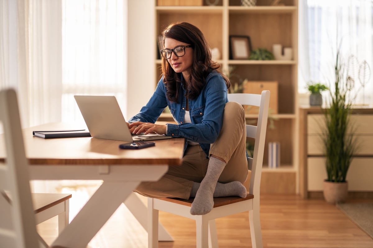 Woman working from home comfortably at a wooden dining table
