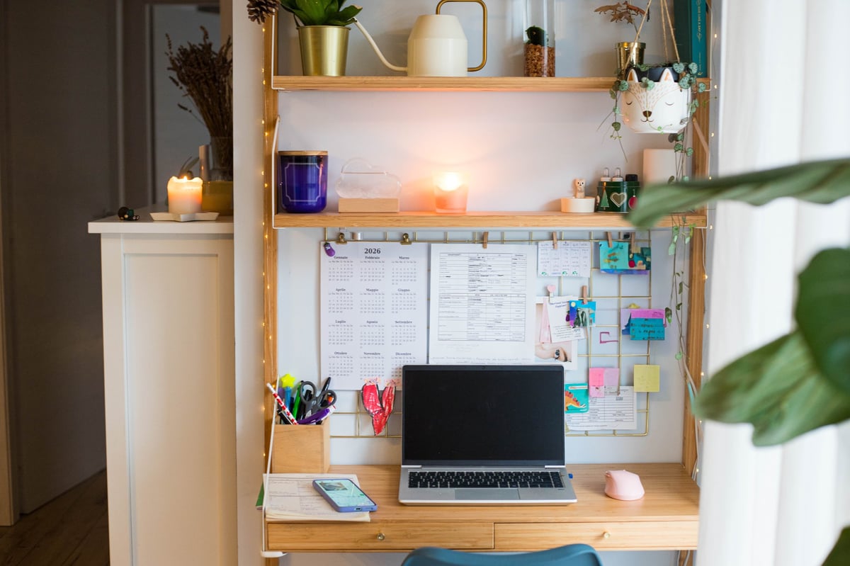 Small home office with laptop, plants, wall board, and candles — personal and lived-in